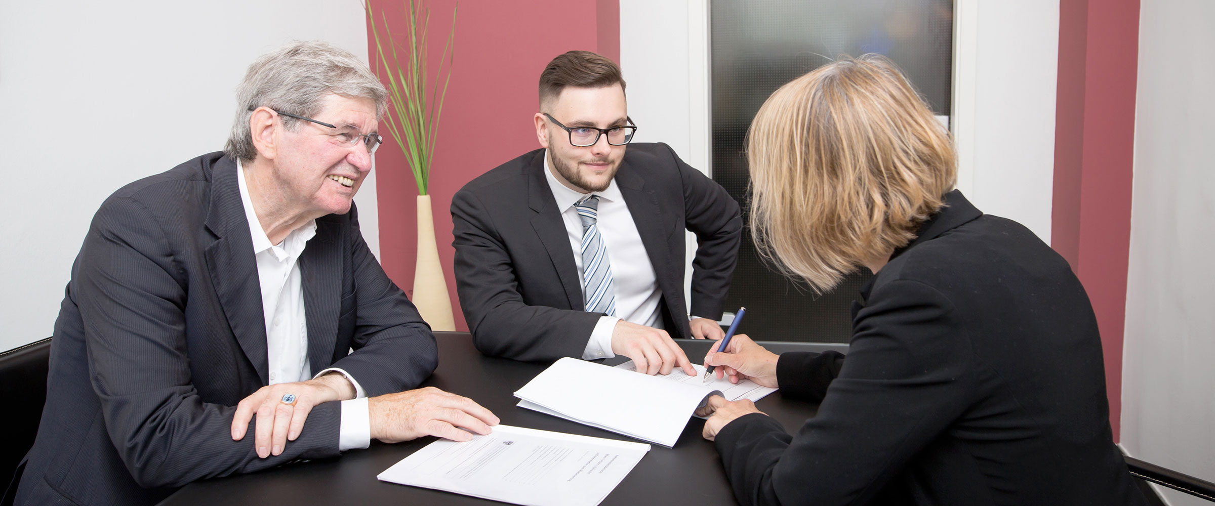 2 Polke und Partner Mitarbeiter sitzen einer Kundin gegenüber, die soeben Verkaufspapiere unterzeichnet.