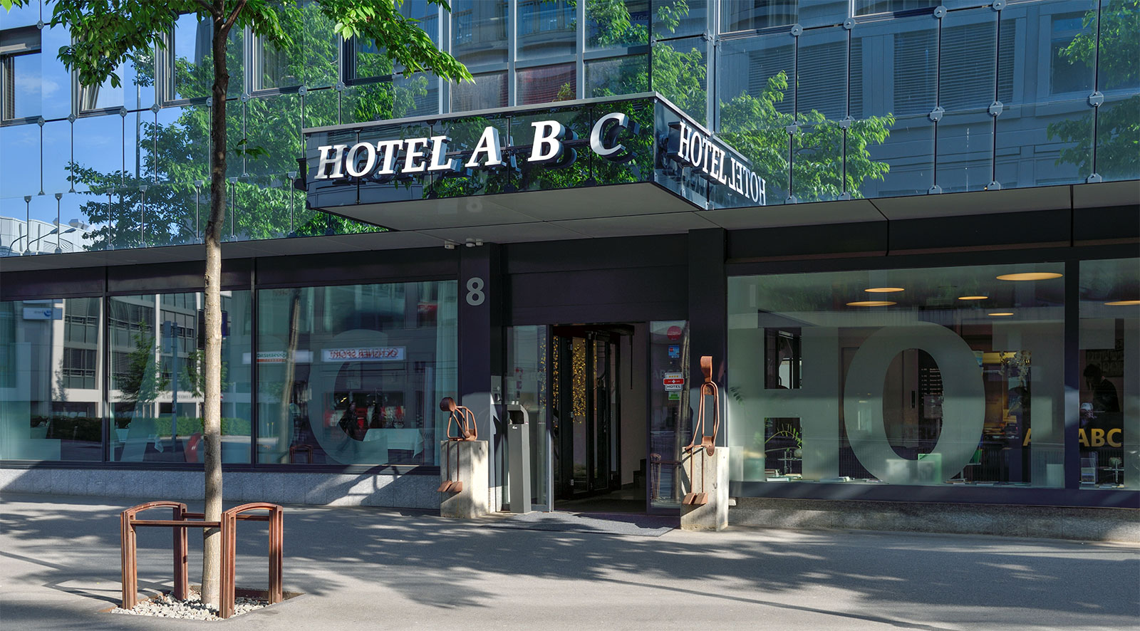 Bild von einem Hotel-Eingang, Glasfasade; über dem Hotel steht "Hotel A B C".